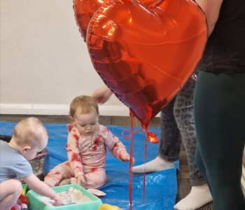 Babies messy playing behind a heart shaped ballon